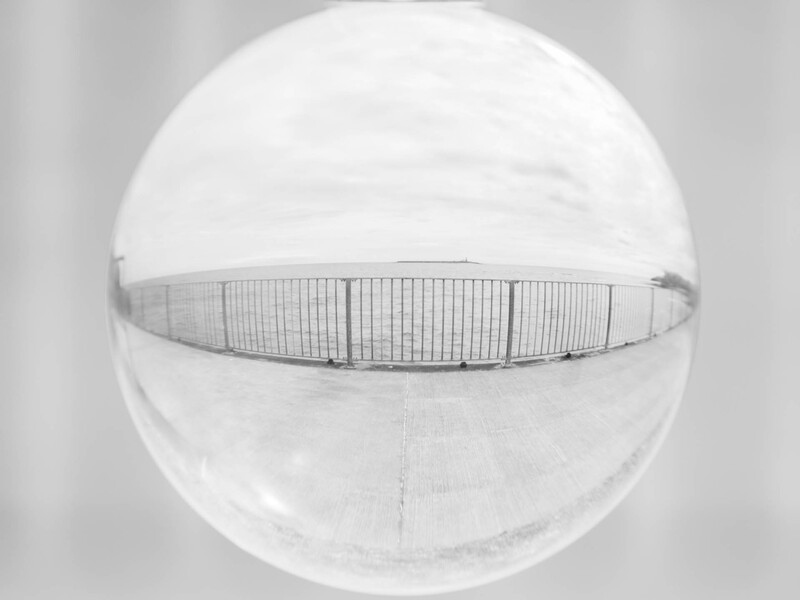 Overhead view of a pedestrian bridge railing cutting horizontally across a spherical architectural dome structure.