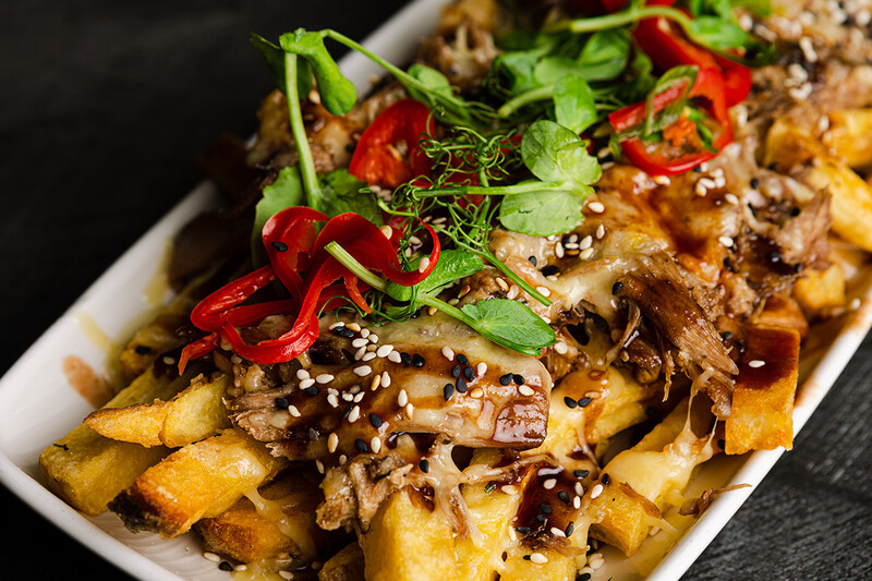 Loaded fries topped with shredded meat, sesame seeds, sliced red chilies, and green onions on a white plate.