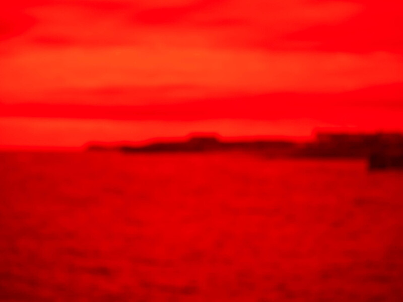 Dramatic red and orange sunset or sunrise over a dark landscape silhouette.