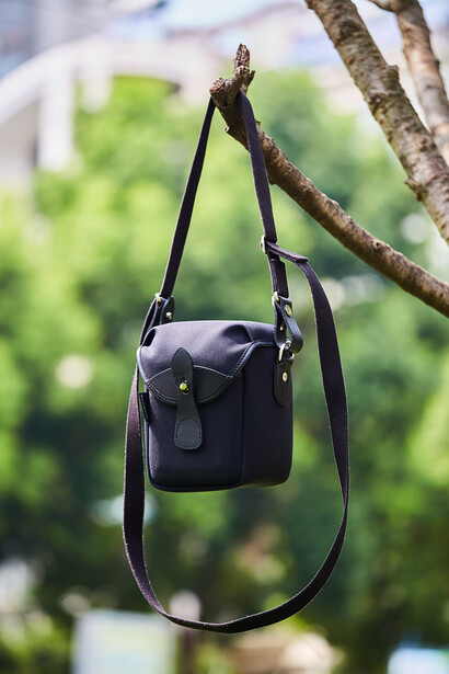 Black canvas shoulder bag hanging from a wooden branch outdoors.