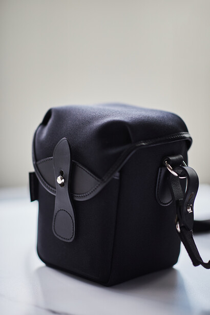 Black leather camera bag with dual compartments and shoulder strap on white surface.