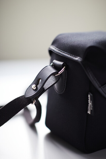Black camera bag with shoulder strap and metal zipper detail on white surface.