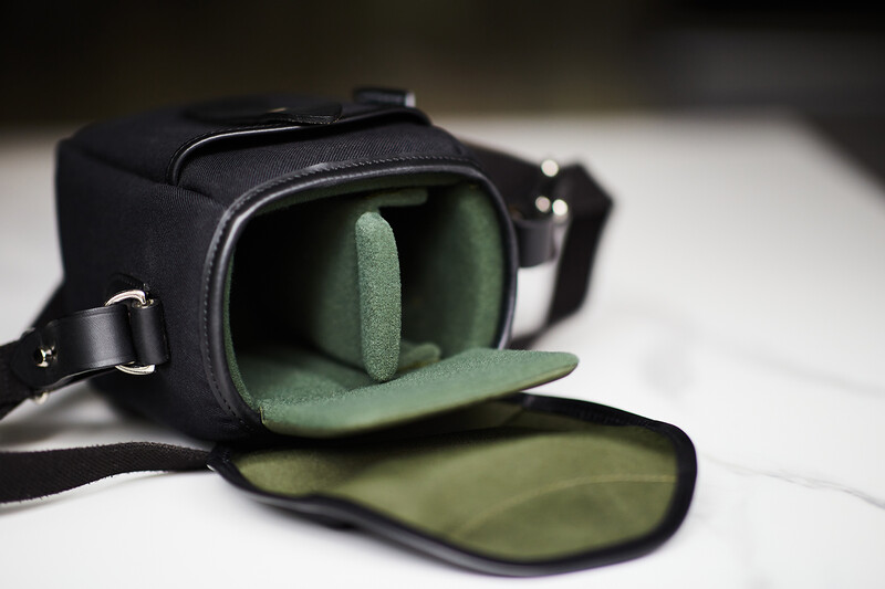 Black camera bag with open flap revealing soft green interior padding and compartment.