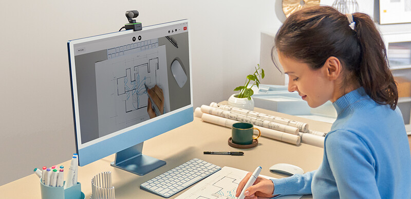 Designer working on architectural floor plan using tablet stylus while referencing blueprints.