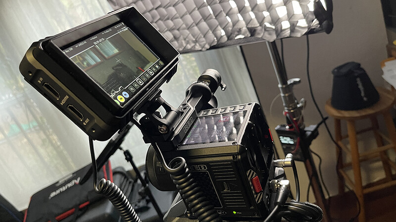Film camera mounted on a tripod with external monitor displaying live footage in a studio setting.