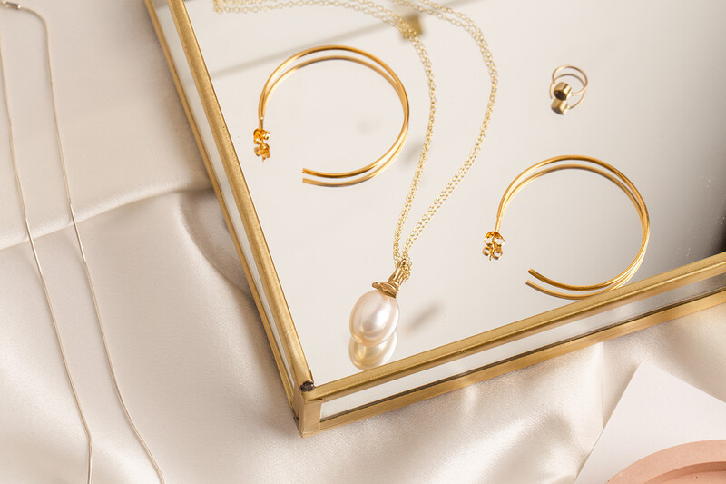Gold jewelry collection featuring pearl pendant necklace, bangle bracelets, and ring arranged on white fabric.