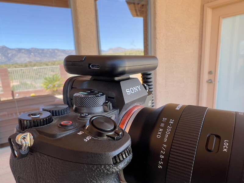Sony mirrorless camera with mounted microphone, lens, and accessories on a sunny balcony overlooking mountains.
