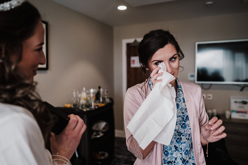 Woman holding tissue to her face while speaking with another person in a modern living room.