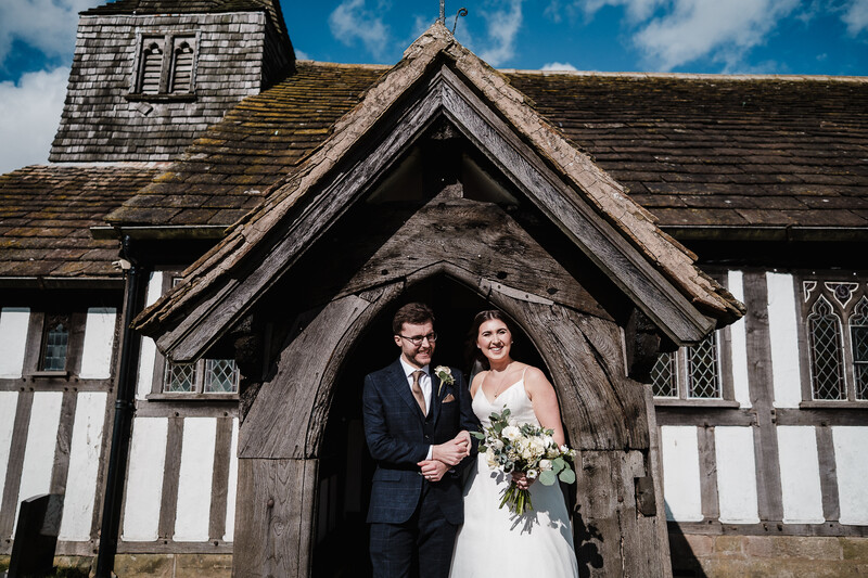 Bride and groom posing in the arched doorway of a historic half-timbered church.