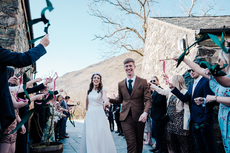 Bride and groom walk together through a cheering crowd during an outdoor wedding ceremony.