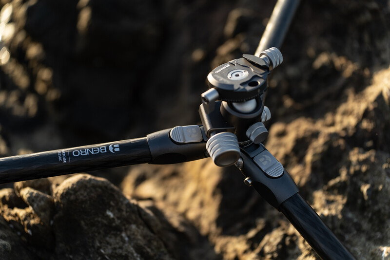 Ball head tripod mount with horizontal arm positioned on rocky terrain in natural sunlight.