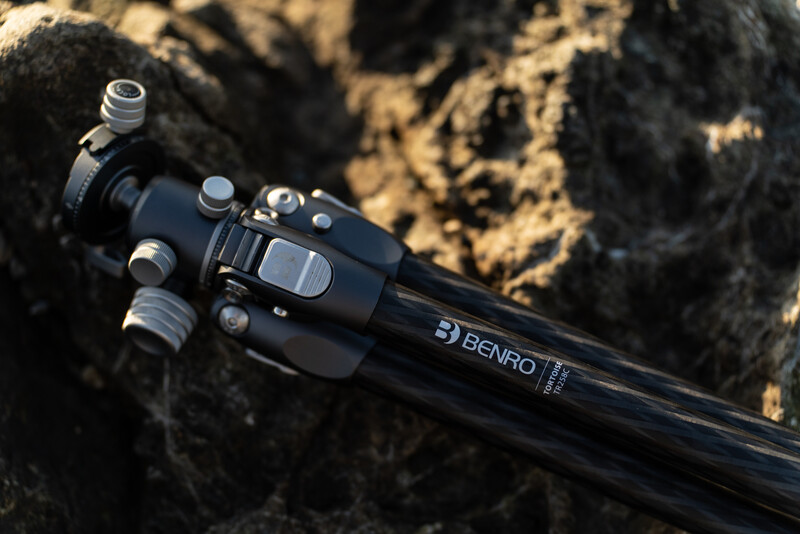 Benro tripod head mounted on a black tripod leg, positioned on a textured rock surface with lichen.