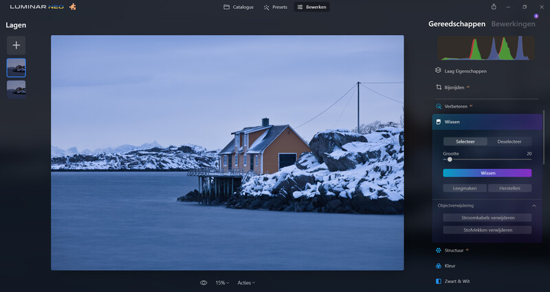 Red brick house with blue trim on snowy rocky shoreline beside calm blue water.