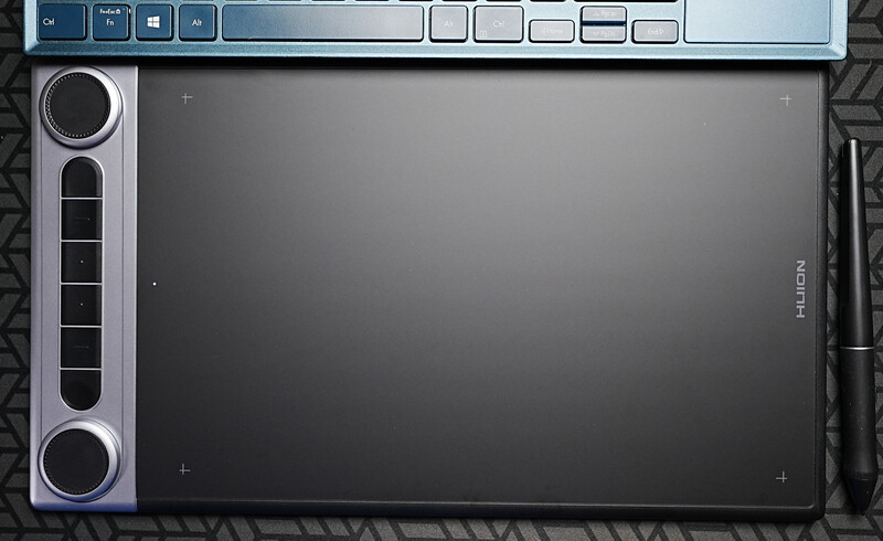 Huion graphics tablet with stylus pen displayed from above on textured surface.