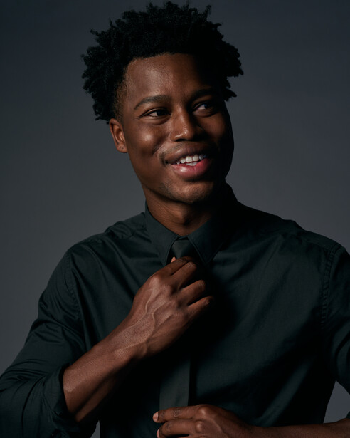 Portrait of a smiling man in a black button-up shirt against a dark gray background.