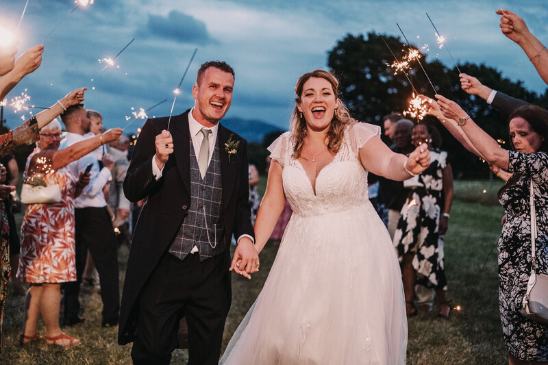 Bride and groom walking hand-in-hand through a sparkler exit at dusk.