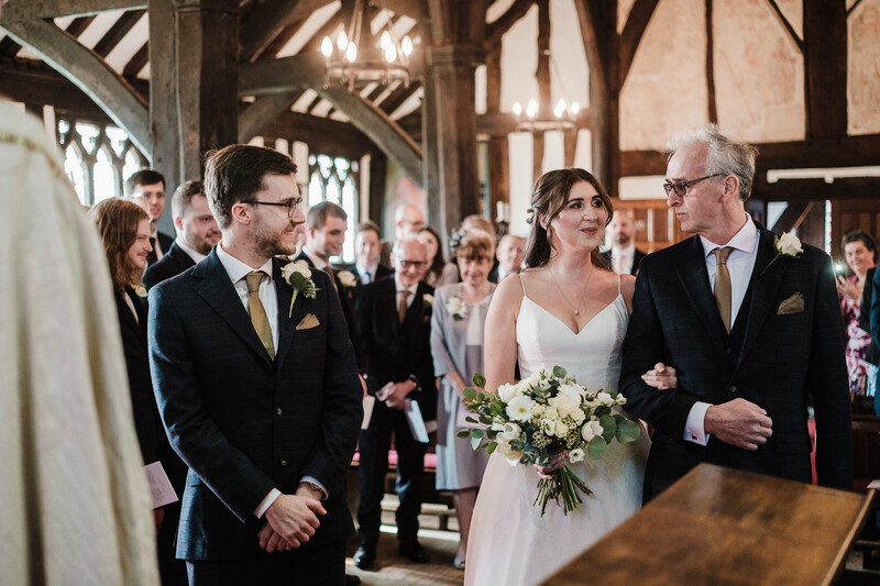 Bride and groom stand with family members during wedding ceremony in timber-framed church interior.