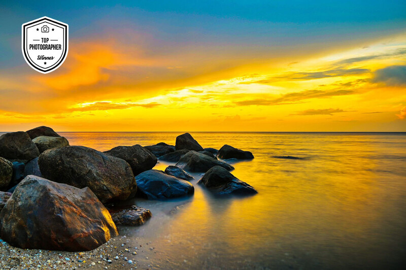 Rocky shoreline with boulders in shallow water during golden hour sunset with dramatic sky.