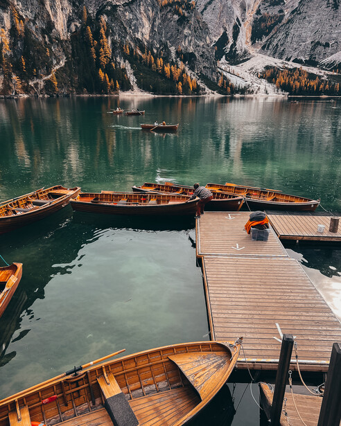 Wooden rowing boats moored at a dock on a turquoise alpine lake surrounded by steep forested mountains.