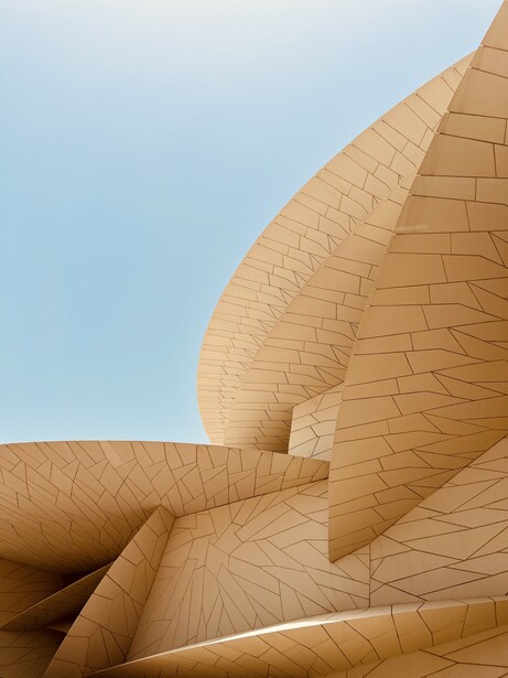 Curved terracotta brick facade with geometric pattern and deep shadows against clear sky.