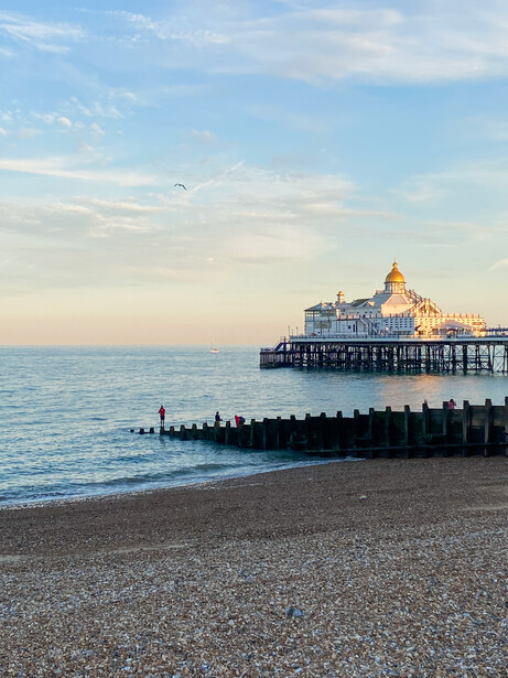 Victorian pier with ornate pavilion extending into calm sea at golden hour, with groyne posts in foreground and pastel sky.