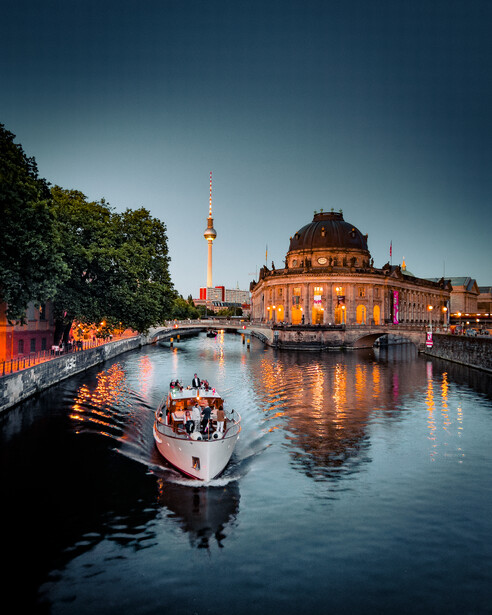 Illuminated riverfront museum building reflected in calm water at dusk with tour boat passing.