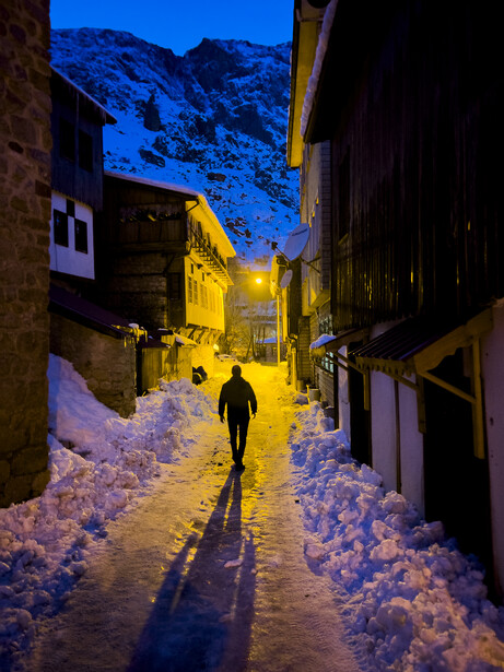 Person jogging through a snow-covered narrow street at twilight with warm golden building lights.