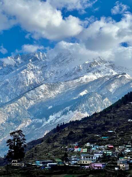 Snow-capped mountain range with forested slopes and scattered buildings in valley below.