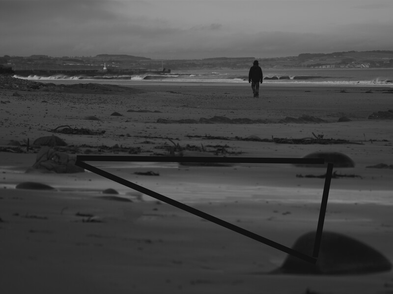 Solitary figure walking along a moody beach scattered with driftwood and debris.