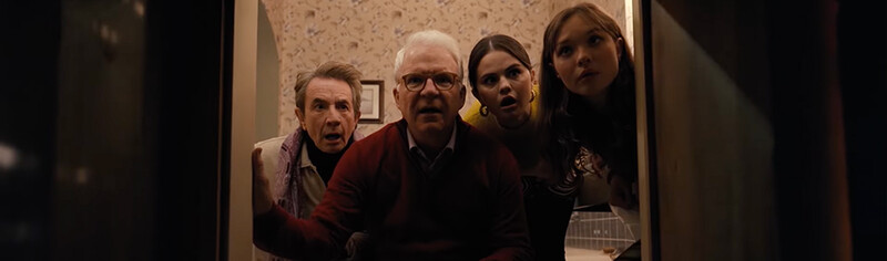 Four people crowded in a doorway with surprised expressions, shot from inside a dimly lit interior space.