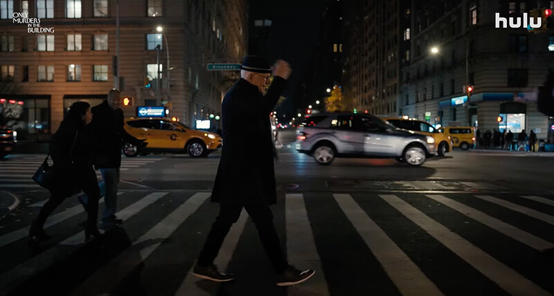 Pedestrians crossing a city street at night on a zebra crossing with yellow taxis and buildings in background.