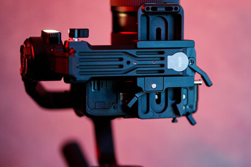 Blue and red mechanical device with ribbed horizontal elements against pink background.