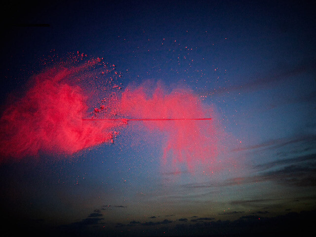 Vivid red powder explosion against twilight sky with silhouetted clouds at horizon.