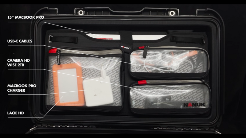 Overhead view of organized gear case with MacBook Pro, chargers, cables, and camera equipment in labeled compartments.