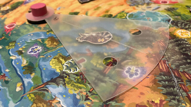 Translucent acrylic spinner wheel overlay on a colorful board game with illustrated flora and fauna elements.
