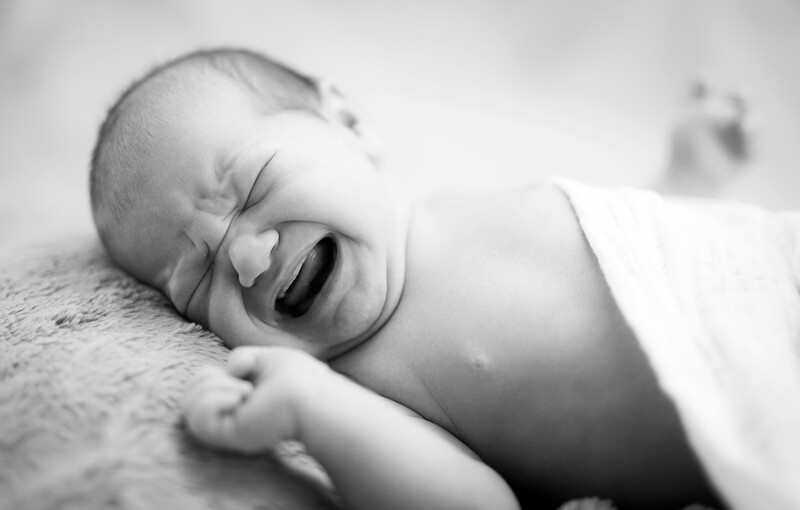 Newborn baby sleeping on textured fabric, captured in black and white.