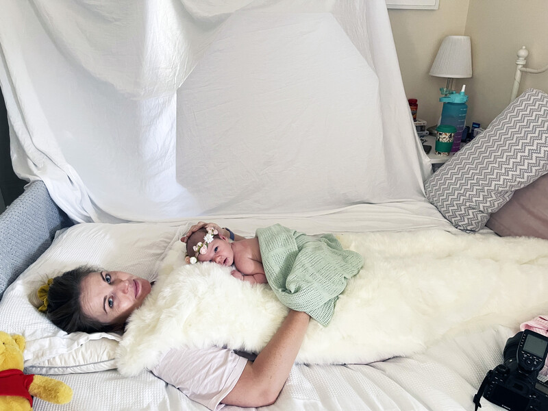 Woman lying on a bed with white bedding, looking at the camera with a relaxed expression.