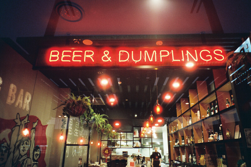 Neon red sign reading "BEER & DUMPLINGS" above a restaurant entrance with warm overhead lighting.