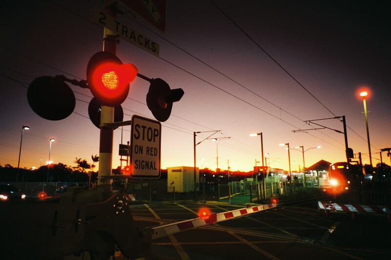Red traffic light glowing at dusk with stop sign and railroad crossing signals at an intersection.