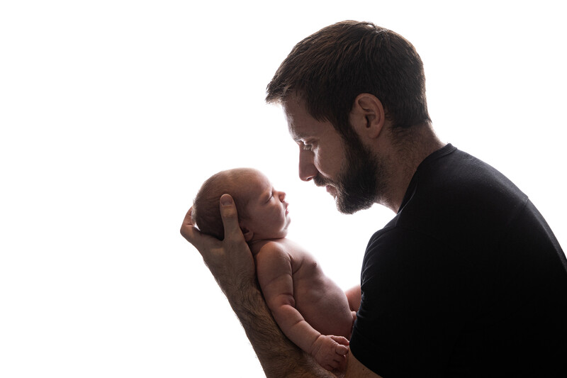 Father holding newborn baby close to his face in tender moment against white background.