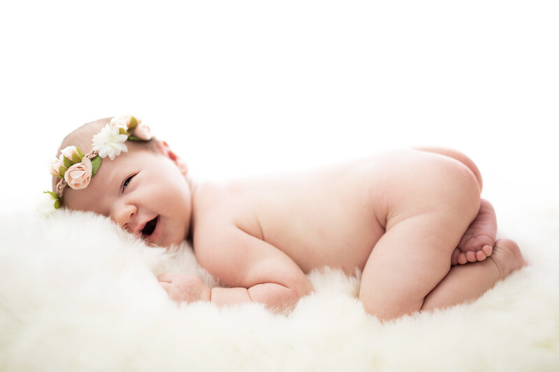 Newborn baby sleeping on white fur wearing a floral crown and tulle.