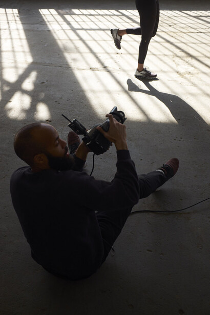 Photographer lying on ground with camera raised overhead, capturing runner's legs in motion above.