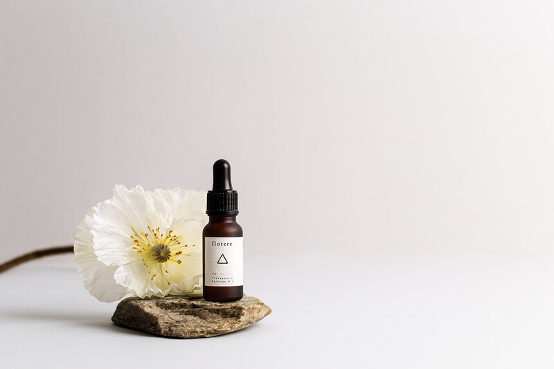 Amber dropper bottle with white flower and textured stone on neutral background.