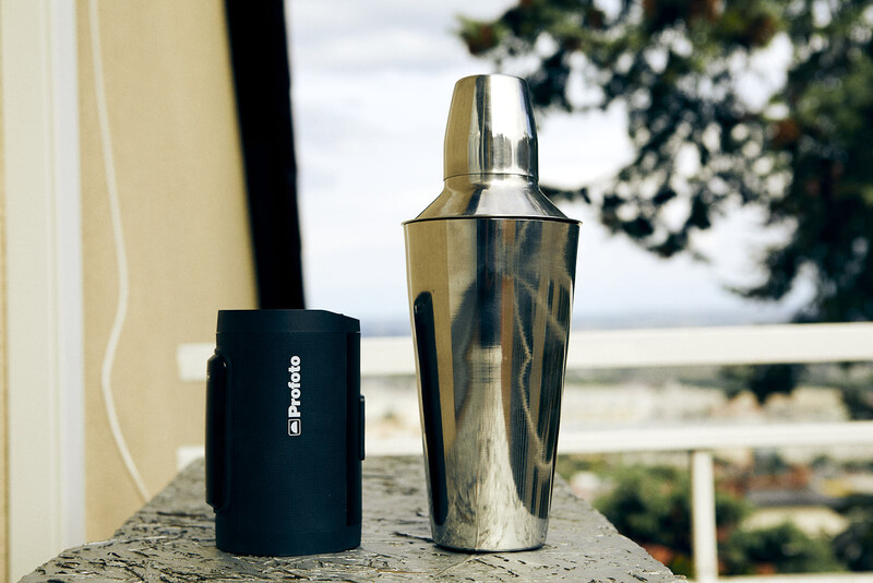 Two cylindrical drinkware items displayed on a concrete surface with a scenic waterfront view in the background.