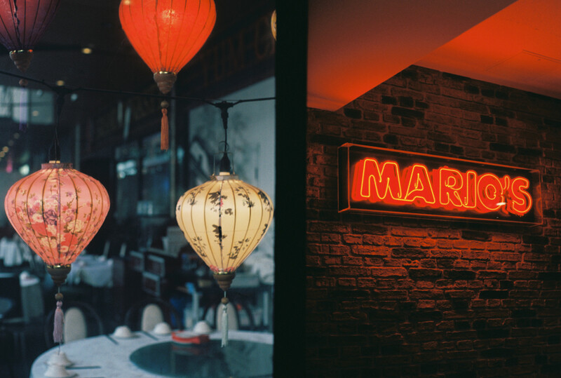 Red and cream silk lanterns hanging in a restaurant window with neon sign glowing behind.