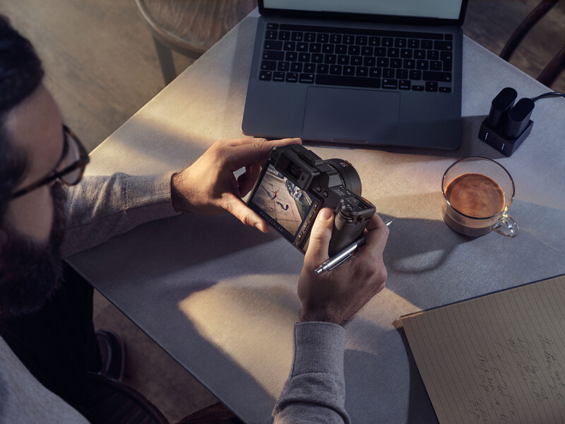 Photographer's hands holding a vintage film camera at a desk with laptop and coffee.