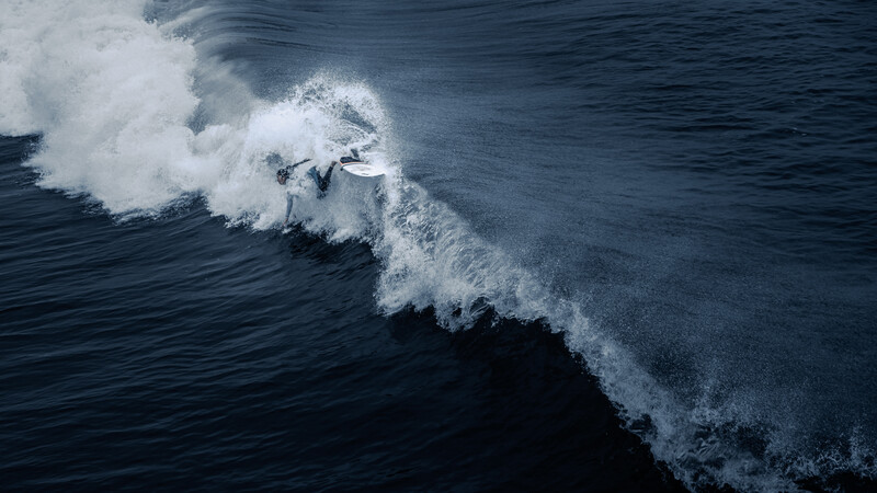 Aerial view of two waves with white foam breaking against dark blue ocean water.