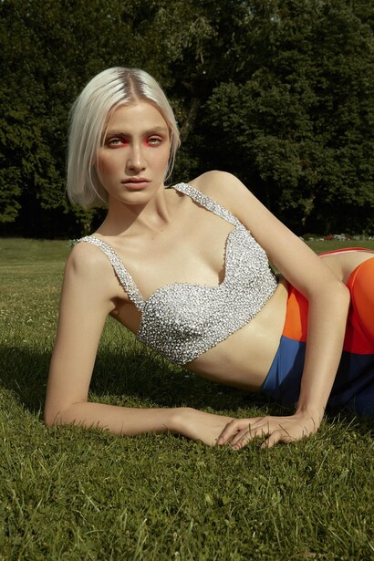 Woman in sparkly crop top and colorful shorts reclining on grass outdoors.