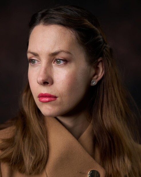 Woman with long brown hair looking downward against dark background.