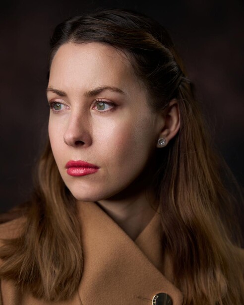 Woman with long brown hair looking downward against dark background.